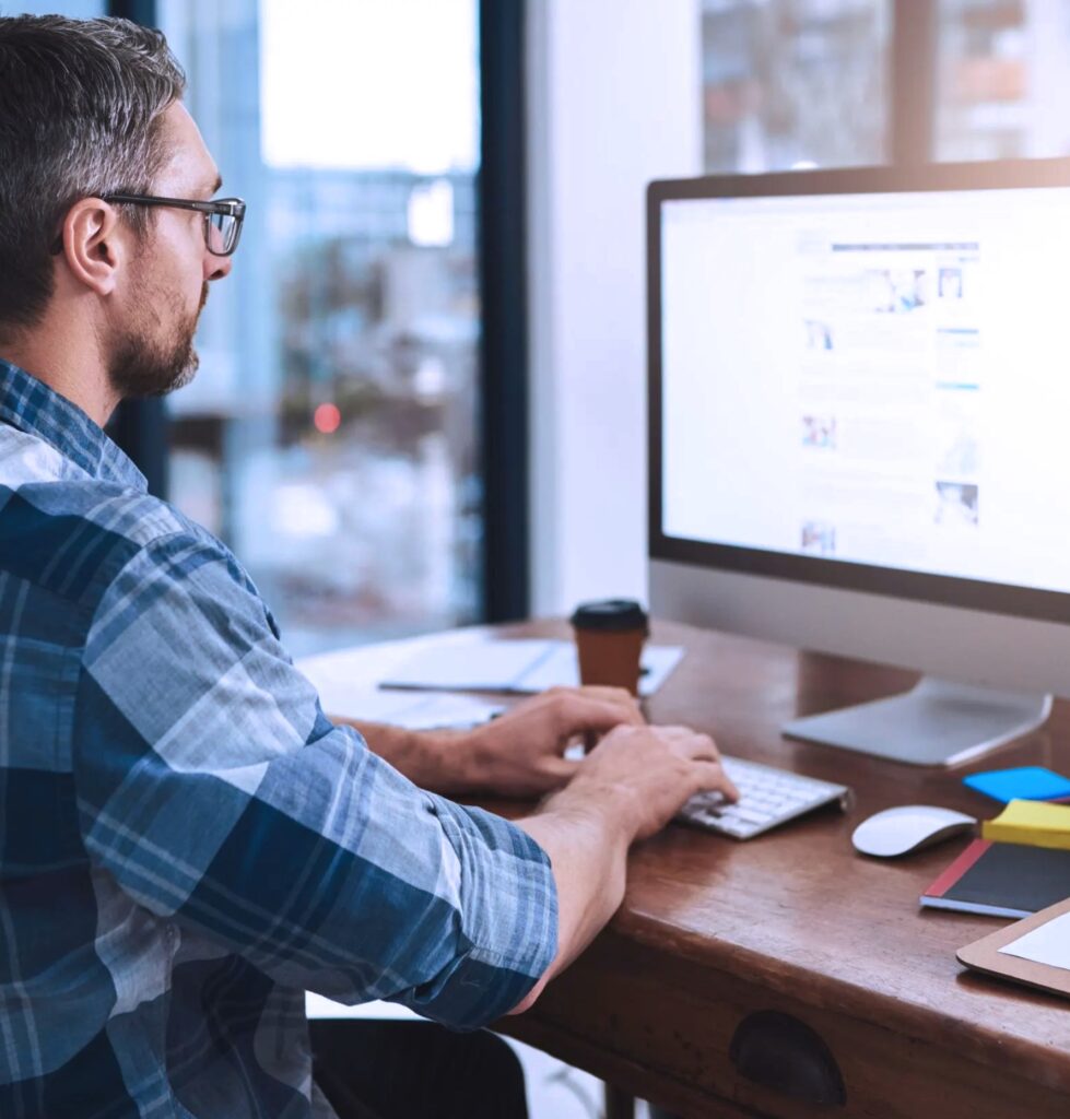 Man working on a computer in a modern office setting, focusing on digital content, relevant to B2B content syndication and marketing strategies.